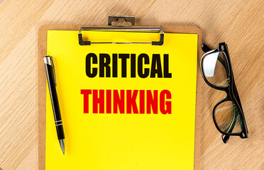 CRITICAL THINKING text on yellow paper on clipboard with pen and glasses