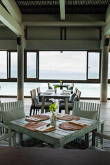 Elegant Seaside Dining Setup Featuring Wooden Tables and Ocean Views in a Tranquil Restaurant Atmosphere.