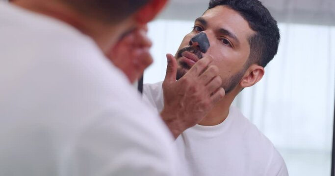 Handsome Asian man uses a nose patch to remove blackheads while standing in front of a mirror.