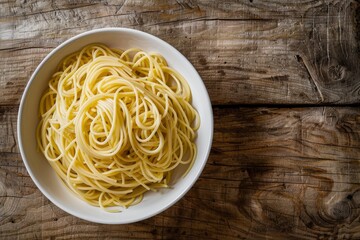 A white bowl filled with spaghetti on a wooden table, top-down view