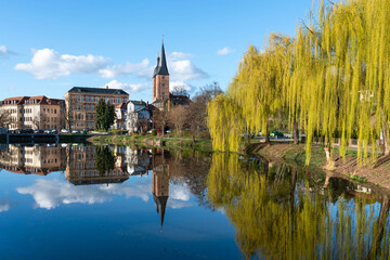 Small pond in the old town of Altenburg Thuringia. The red tips in the reflection on the water surface. Landmark of Altenburg. Spring landscape with flowering willows. - obrazy, fototapety, plakaty