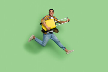 Full length profile photo of overjoyed person hands hold suitcase jump empty space isolated on green color background