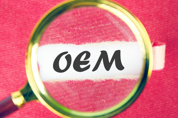 OEM original equipment manufacturer concept. Text through a magnifying glass under a torn piece of...