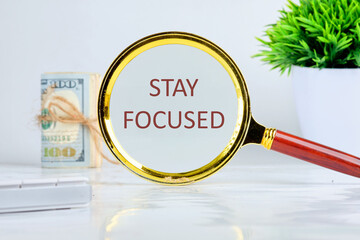 Motivation concept. STAY FOCUSED through a magnifying glass on a gray background, a roll of banknotes and a green plant in the background