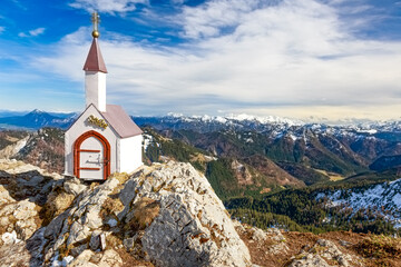 Weiß getünchte Miniatur Kapelle auf dem Hochgern Gipfel in den Chiemgauer Alpen unter teilweise...