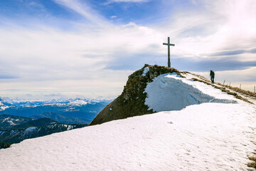 Ein Wanderer läuft zum Hochgern Gipfelkreuz über einen schneebedeckten Bergrücken, in den Chiemgauer Alpen in Bayern Deutschland