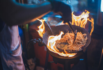 An outdoor street food chef expertly frying noodles in a flaming wok, capturing the energy of street cuisine..