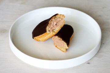Chocolate eclair cut in half, showing creamy filling, on white plate. Gourmet chocolate glazed...