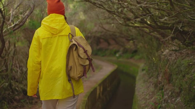 A girl in a yellow jacket travels with a backpack and visits extraordinary places and trails on the island of Madeira, Levada dos Tornos, Portugal