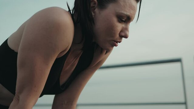 Exhausted athletic woman pausing to rest after a running session at sunset, showing determination and fatigue.