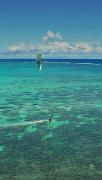 Aerial view kitesurfer speeding with kite in clear crystal water from drone. An athlete rides a kite in the Indian Ocean on the island of Mauritius. Live reef near island. Conquest of the sea