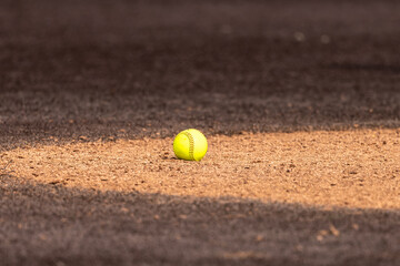 Optic yellow softball on clay pitchers circle with brown synthetic turf	
