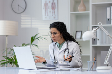 A professional Latino woman doctor is focused on her work, consulting medical information on her...