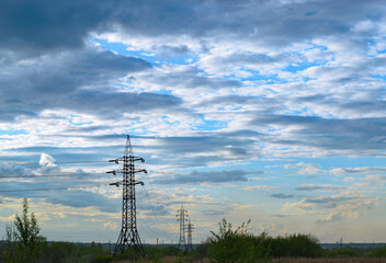 A row of power lines in a field under a cloudy sky