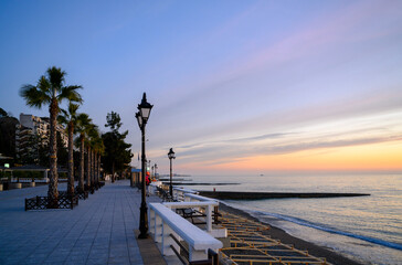 The sea embankment with palm trees and lanterns at sunset