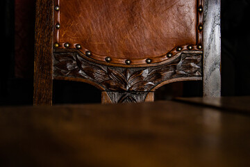 Close up of the detail of antique wooden Chair covered with brown leather upholstery, decorated...