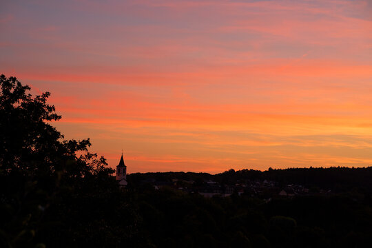 Silhouette of village and forest against sunset sky