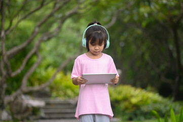 Cute girl in casual clothes Use headphones and learn from your digital tablet in the park.