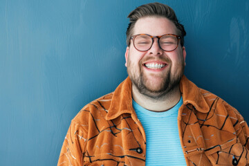 Man enjoys a light moment laughing in an orange textured jacket against a blue background,...