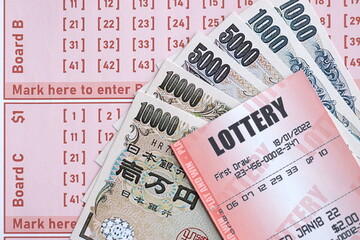 Lottery tickets lies with japanese yen bills on gambling sheets with numbers for marking to play lottery. Lottery playing concept or gambling addiction