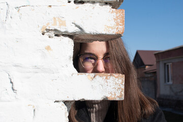 A woman in glasses looking through the bricks of an old brick wall	