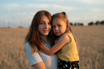 A mother and his daughter in field at sunset	