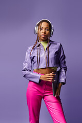 pretty african american woman with headphones holding laptop and standing on purple background © LIGHTFIELD STUDIOS