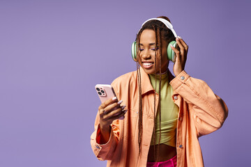 happy african american woman listening music in her headphones and using phone on lilac backdrop - 773249492