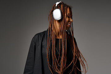 joyful and young African American woman in 20s with headphones listening to music on grey backdrop