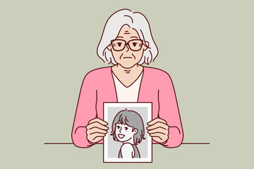 Elderly woman remembers youth, showing portrait from past, and looks at screen with slight sadness. Elderly lady with gray hair shows photo of herself from childhood, wishing she could turn back time.