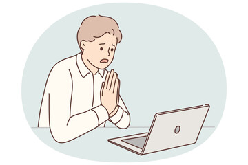 Man manager prays sitting at table with laptop asking god for help after making mistakes in project