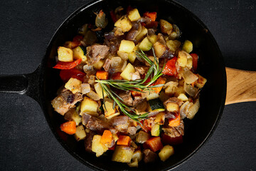 Top view of a hearty skillet beef ragout with mixed vegetables on a textured black backdrop