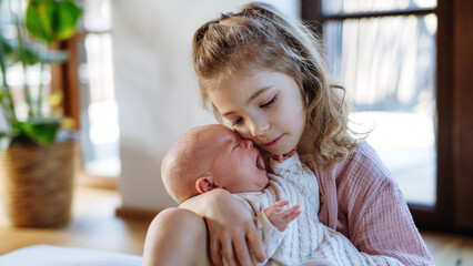 Fototapeta premium Portrait of big sister soothing newborn sister. Girl taking care of crying baby. Sisterly love, joy for new family member.