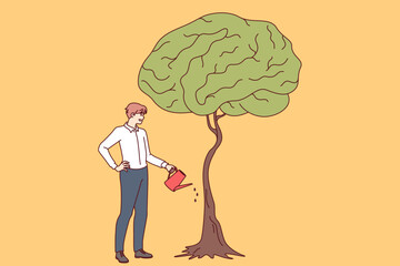 Businessman develops own intelligence by watering trees with brain shaped leaves as metaphor for receiving business education. Guy entrepreneur cares about gaining new knowledge and developing brain