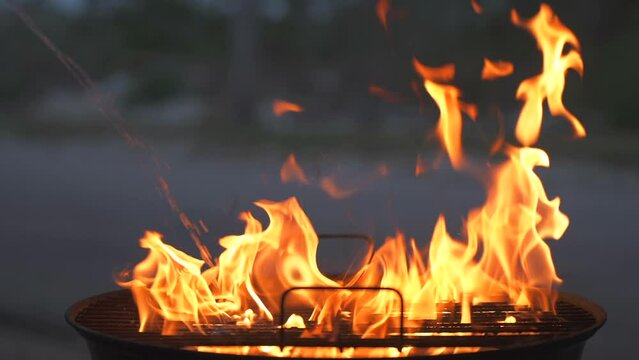 Close up slow motion of charcoal lighter fluid stream add to the fire in a barbecue grill and flame flare strong. BBQ and grilling safety tips