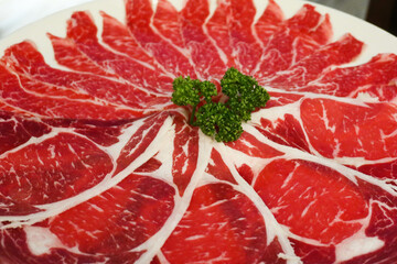 close up of sliced raw beef ingredient with white fat on a white round plate ready for hotpot cooking
