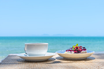 Coffee cup and blueberry cheese pie with beautiful sea beach background in the summer time.