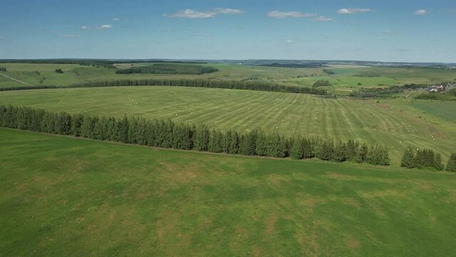 The camera slowly rises above a green field revealing a view of twisted haystacks