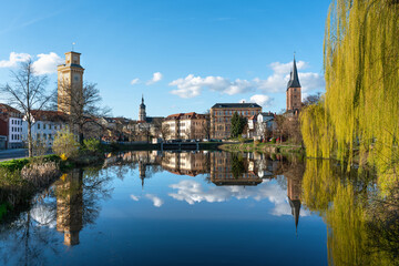 Small pond in Altenburg. Beautiful reflection on the water surface. Art tower, red tips and the tower of the town hall in the picture. Spring weather in Altenburg Thuringia. - obrazy, fototapety, plakaty
