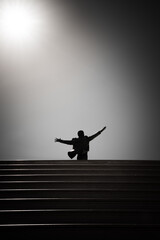 Silhouette of a man standing on the stairs and raising his hands. Statue of Domenico Modugno. Polignano a Mare, Italy - obrazy, fototapety, plakaty