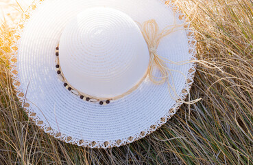 Sunlit beach hat placed on golden dry grass creating interesting curls and shapes for copy space area. Summer concept