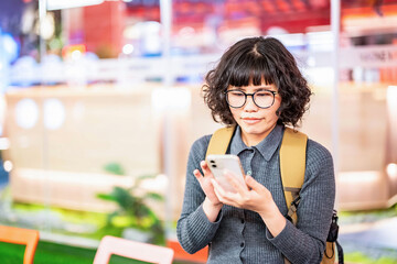 Woman waiting in line outside restaurant and playing with mobile phone