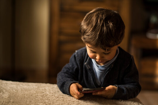 Baby one year old boy touching smartphone at home living room.