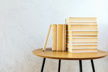 Pile of books neatly arranged on top of a rustic wooden table against white wall. With copy space.