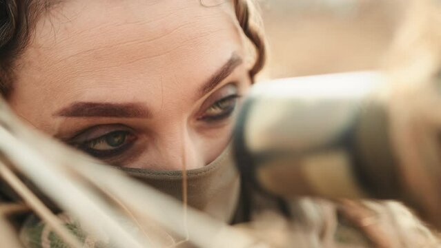 A female sniper lies motionless in position, her eyes solely focused through the optical scope, the epitome of stillness and patience as she awaits the opportune moment to engage her target.
