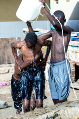 jeune garçon se verse de l'eau du puit en Afrique occidentale - obrazy, fototapety, plakaty