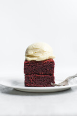 Fudgy red velvet brownies with cream cheese ice cream on a white plate