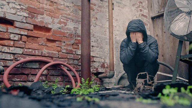 Man crouching in abandoned building warehouse with frustrated anger rage. Homeless, depression, mental illness.