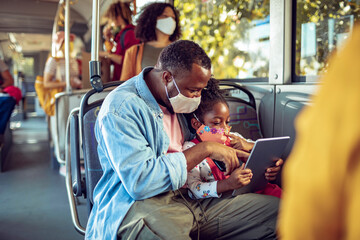 Father and daughter in face masks using tablet on public bus