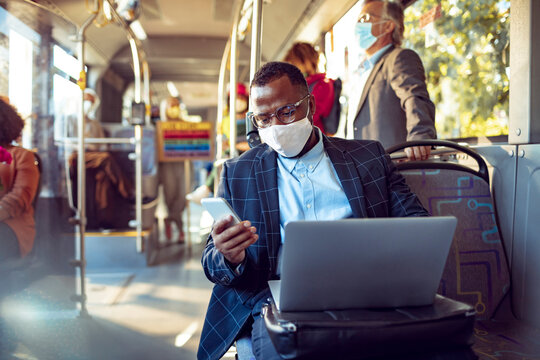 Businessman with face mask working on laptop on public transport